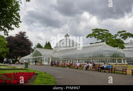 Leute sitzen auf Bänken genießen die warmen Temperaturen im Sommer im Botanischen Gärten in Glasgow, Schottland, Großbritannien. Stockfoto