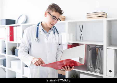 Ein junger Arzt in ein weißes Gewand steht in der Nähe des Racks und halten einen Ordner mit Dokumenten. Stockfoto