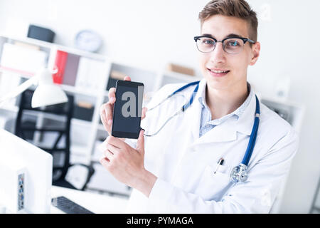 Ein junger Mann in einer weißen Robe steht im Büro und ein Telefon. Stockfoto