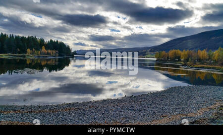 Meditation in eine stille Kieselstrand mit einer wunderschönen ländlichen Blick auf einem ruhigen See, Berge, Falllaub und dramatische Wolkenhimmel. Stockfoto