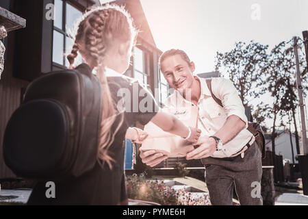 Dunkelhaarige Schülerin tragen Rucksack vorhanden vom Vater empfangen Stockfoto