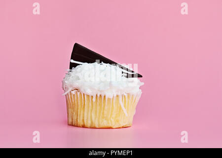 Ziemlich coconut frosted Cupcake mit einem Keil von Schokolade gegen einen rosa Hintergrund eingerichtet. Stockfoto