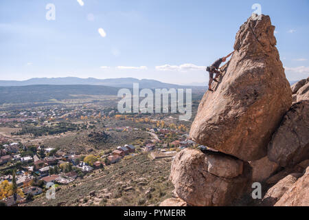 La Pedriza, Madrid, Spanien. Männliche Kletterer beginnt der letzte Teil einer Granit Felsen ähneln einem Turm mit Dorf im Hintergrund. Stockfoto