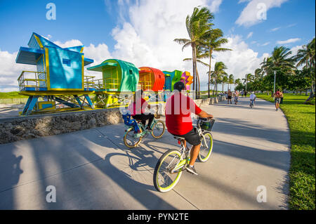 MIAMI - ca. September 2018: ein paar Fahrräder fahren vorbei an einer Reihe von bunten Rettungstürme warten auf Platzierung in South Beach. Stockfoto