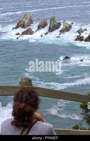 Gueirua Strand, Asturien, Spanien. Vertikale Ansicht von touristischen Frau beobachten die rauhe See brechen im Riff. Stockfoto