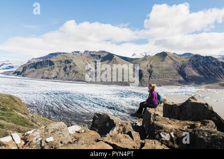 Frau sitzt auf Felsen mit Blick auf Skaftafellsjokull Teil des Vatnajökull Gletscher im Nationalpark Skaftafell, Island. Stockfoto