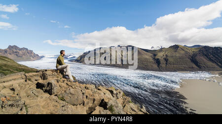 Mann sitzt auf Felsen mit Blick auf Skaftafellsjokull Teil des Vatnajökull Gletscher im Nationalpark Skaftafell, Island. Stockfoto