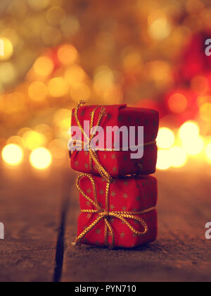 Two red Christmas gift boxes stacked on a wooden table, blurred Christmas lights in the back, selective focus on foreground Stockfoto