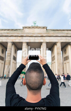 Nahaufnahme eines jungen kaukasischen Mann, von hinten gesehen, ein Bild von der beliebten Brandenburger Tor in Berlin, Deutschland, mit seinem Smartphone Stockfoto