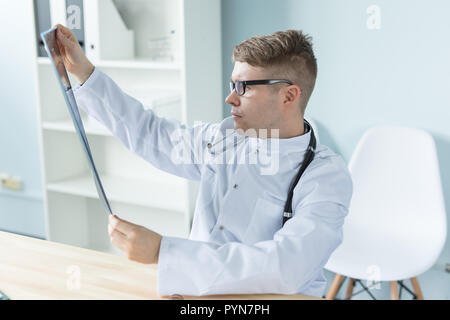 Junge kaukasier Arzt sitzt in seinem Büro und suchen X-ray Image Stockfoto