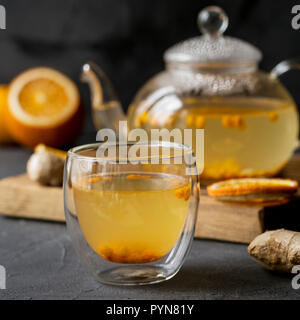 Warme Meer buck Thorn Tee Teekanne aus Glas mit Glas Schale, Orange und Ingwer in der Nähe, auf Holzbrett auf schwarzem Hintergrund Stockfoto