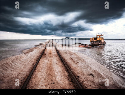 Alten rostigen Bahngleise auf einem Hügel in Salt mining Lake in der Nähe von Salzwasser. Alten verrosteten Traktor in Salz ins Wasser geworfen, Stockfoto