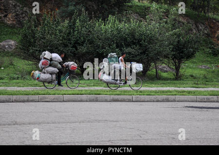 09/07/2018, Kaesong, North-Korea: Zwei hoffnungslos überlastet Bikes sind die Pedale in Richtung Stadt. Wer ein Fahrrad ist ein glücklicher Mann in Nordkorea. Stockfoto