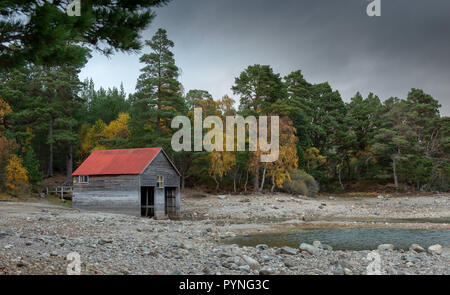 Ein red-roofed Bootshaus am Ufer des Loch Vaa in den schottischen Highlands, im Herbst mit den Bäumen ihre hellen Farben angezeigt. Stockfoto