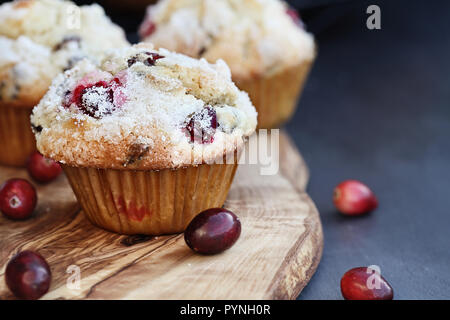 Cranberry Muffins mit Zitrone Zucker Belag auf einem urigen Schneidbrett mit Losen Beeren. Extrem flache Tiefenschärfe mit selektiven Fokus auf Muffin Stockfoto