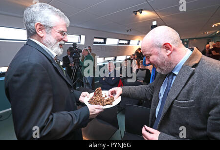 Der ehemalige Sinn-Fein-Führer Gerry Adams überreicht dem Journalisten Brian Rowan Christmas Pudding bei der Vorstellung seines Rezepturbuches mit dem Titel "The Negotiators' Cookbook" im Culturlann on the Falls Road in Belfast. Stockfoto