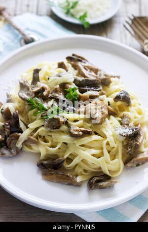 Tagliatelle mit Sahne und Waldpilzen Soße in eine weiße Platte auf einem hölzernen Hintergrund. Im rustikalen Stil. Stockfoto