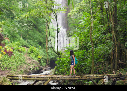 Touristische Frau Bambus Überqueren einer Brücke in der Nähe des Red Coral Munduk Wasserfall im Dschungel, Bali, Indonesien Stockfoto