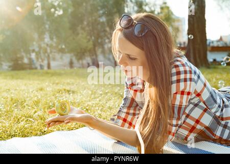 Junge Frau mit Wecker in Ihrer Hand. Hintergrund sunny City Park, Kopieren, goldenen Stunde. Stockfoto