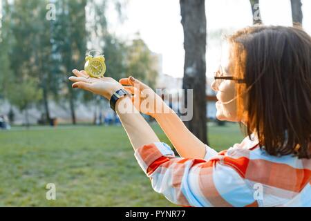 Wecker in weiblicher Hand, Hintergrund grünen Gras im Park, Sonnenlicht, Kopie, goldenen Stunde. Stockfoto