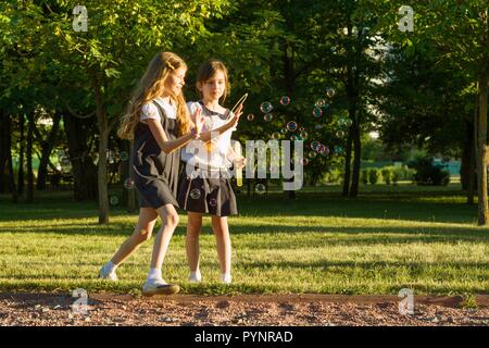 Zwei kleine Mädchen Freunde Schulmädchen 7-8 Jahre alte Spiel mit Seifenblasen auf der Wiese im Park Stockfoto