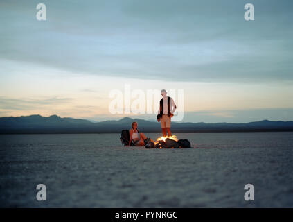 Abenteuerlustige junge Paar um ein Lagerfeuer in einem abgelegenen Wüste. Stockfoto