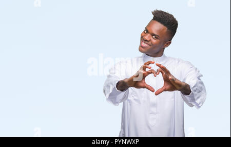 Junge arabische afrikanischen Mann mit traditionellen djellaba über isolierte Hintergrund in der Liebe mit Herz und mit Hand lächelnd. Romantische con Stockfoto