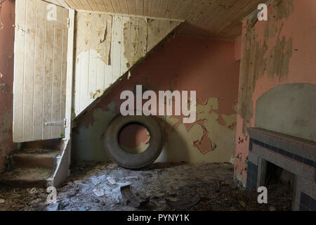 Treppenhaus, mit alten Reifen unter, in einem alten verlassenen Hütte. Stock mit geschälten Farbe und Tapete verstreut, mit alten Kamin auf der einen Seite. Stockfoto