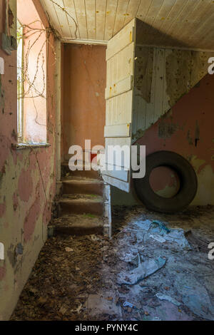 Treppenhaus, mit alten Reifen unter, in einem alten verlassenen Hütte. Farbe und Tapete auf der Etage, Tür zur Treppe öffnen, Licht vom Fenster geschält. Stockfoto