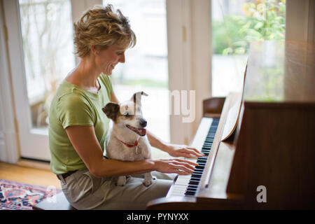 Lächelnd Mitte der erwachsenen Frau ein Klavier spielen mit Ihrem Hund auf dem Schoß. Stockfoto