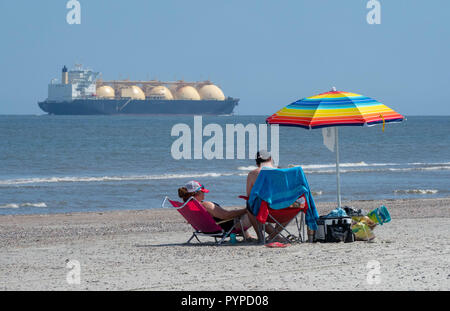 Paar Entspannen am Strand in Tybee Island als gigantische Flüssiggas Containerschiff in den Atlantik - Savannah Georgia USA Kreuzfahrten Stockfoto