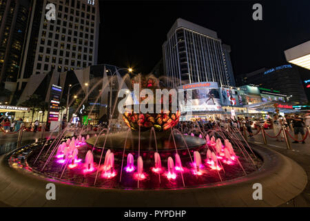 KUALA LUMPUR, 16. August 2018 - Bunte Brunnen vor der beschäftigt und überfüllten 'Pavilion' Einkaufszentrum der Stadt bei Nacht Stockfoto