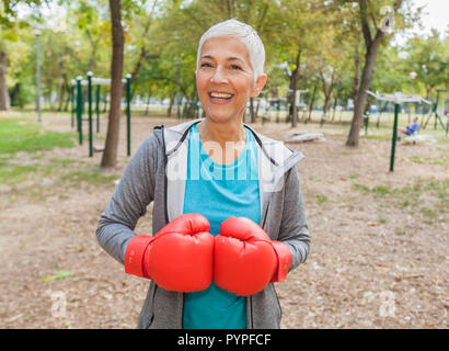 Portrait von Passen ältere Frau mit Boxhandschuh Der Outdoor Fitness Park in Sportbekleidung. Aktive alte Menschen zu einem gesunden Lebensstil Stockfoto