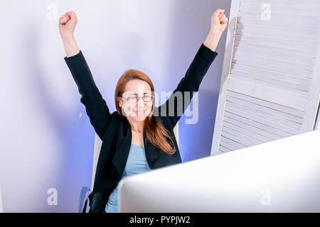 Porträt der glückliche junge erfolgreiche Geschäftsfrau feiern etwas mit den Armen oben im Büro. Positive Emotion. Big Deal, Förderung, Lotterie gewinnen oder Dis Stockfoto