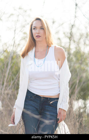 Eine junge Frau posiert im Feld Öffnen ein weißes Hemd und Jeans Stockfoto