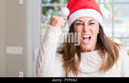 Frau mittleren Alters tragen Santa Claus hat zu Hause genervt und frustriert schrie mit Zorn, verrückt und schreien mit erhobener Hand, Wut Konzept Stockfoto