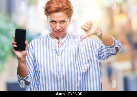 Attraktives senior kaukasischen rothaarige Frau, der Bildschirm des Smartphones über isolierte Hintergrund mit Verärgerten Gesicht, negatives Vorzeichen zeigen Abneigung mit dem Daumen Stockfoto