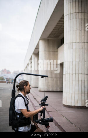 Professionelle Videofilmer holding Kamera auf 3-Achs Gimbal, die auf einfache Rig montiert. Videofilmer mit Steadicam. Pro Ausrüstung hilft Video in hoher Qualität ohne Schütteln zu machen. Stockfoto