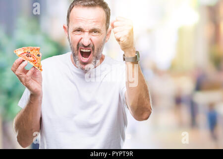 Mittleres Alter hoary älterer Mann essen Pizza über isolierte Hintergrund genervt und frustriert schrie mit Zorn, verrückt und schreien mit erhobener Hand Stockfoto