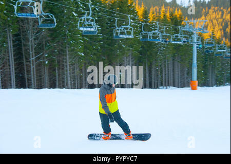 Junge reiten Snowboard, Skilift und Tanne sonnigen Wald im Hintergrund, Bukovel, Ukraine Stockfoto