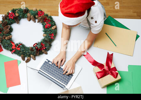 Frau in Santa Hut mit der Eingabe auf Laptop Stockfoto