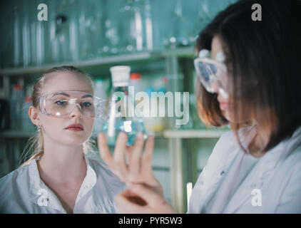 Zwei junge Frau im chemischen Labor, die eine klare Flüssigkeit in Flaschen mit. Blonde Frau im Fokus Stockfoto