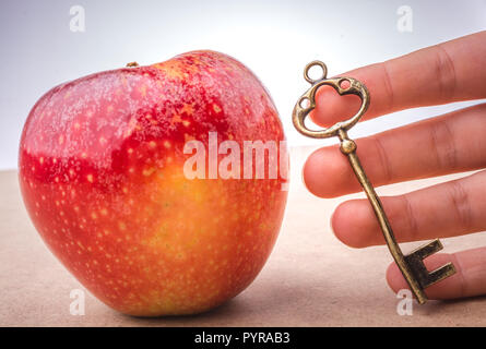Hand mit einem Schlüssel neben einem roten Apfel Stockfoto