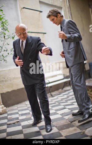 Senior Business mann Lehre in der Mitte des erwachsenen männlichen Kollegen in einem Innenhof zu tanzen. Stockfoto