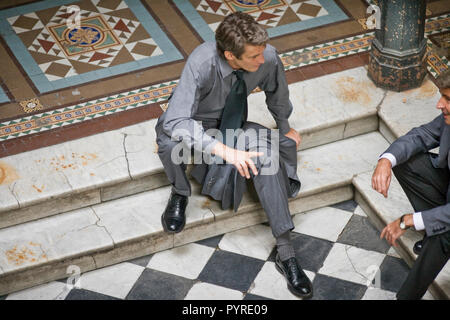 Mitte - erwachsener Mann sitzt auf einen Schritt, während im Gespräch mit einem männlichen Freund in einem Foyer. Stockfoto