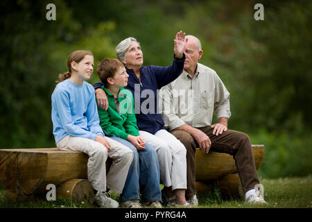 Senior Paar mit ihren zwei Enkelkindern auf Holzbank. Stockfoto