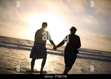 Paar Hände halten bei einem Spaziergang am Strand bei Sonnenuntergang. Stockfoto