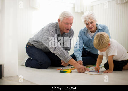 Junge Junge sitzt auf dem Boden mit seinen Großeltern und Zeichnen mit Buntstiften. Stockfoto