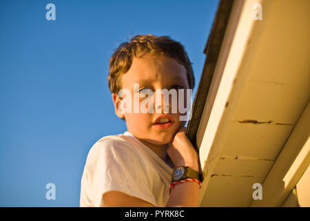 Porträt eines Jungen Festhalten am Rande eines Dach im Freien unter der Sonne. Stockfoto