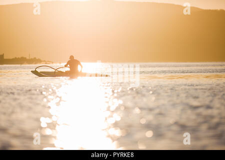 Mann in einem Kajak paddeln auf einem See bei Sonnenuntergang. Stockfoto